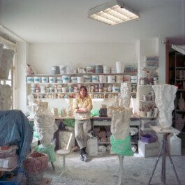 Sarah Pschorn in her ceramic studio in Leipzig. She is standing in the center surrounded by her sculptures.
